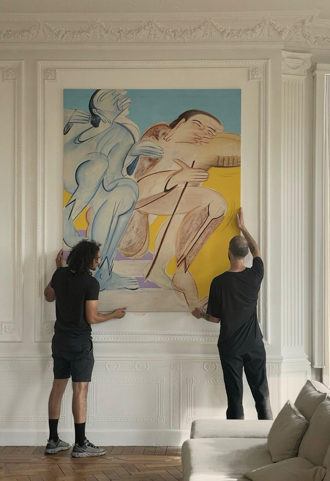 Two art handlers hanging a large figurative painting in a panelled Haussmann interior